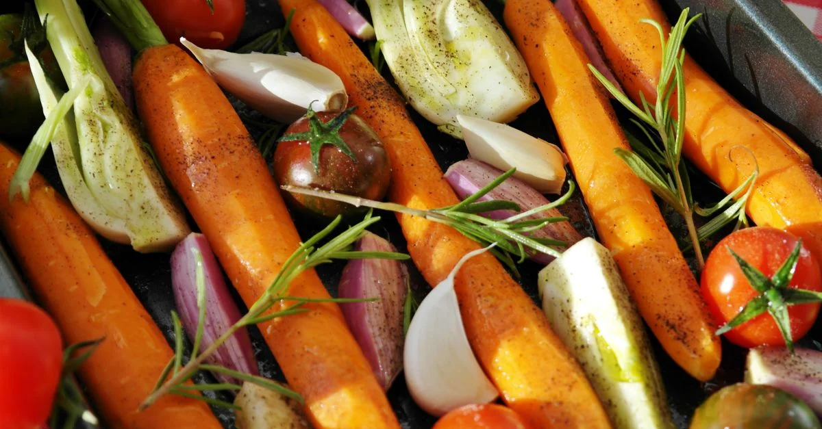 Des légumes colorés prêts pour la cuisson, comprenant des carottes, des tomates et des herbes.