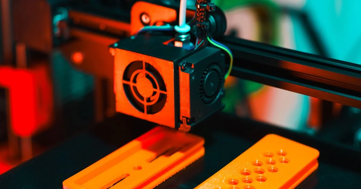 Vue détaillée d'une imprimante 3D en action, extrudant des composants en plastique orange.